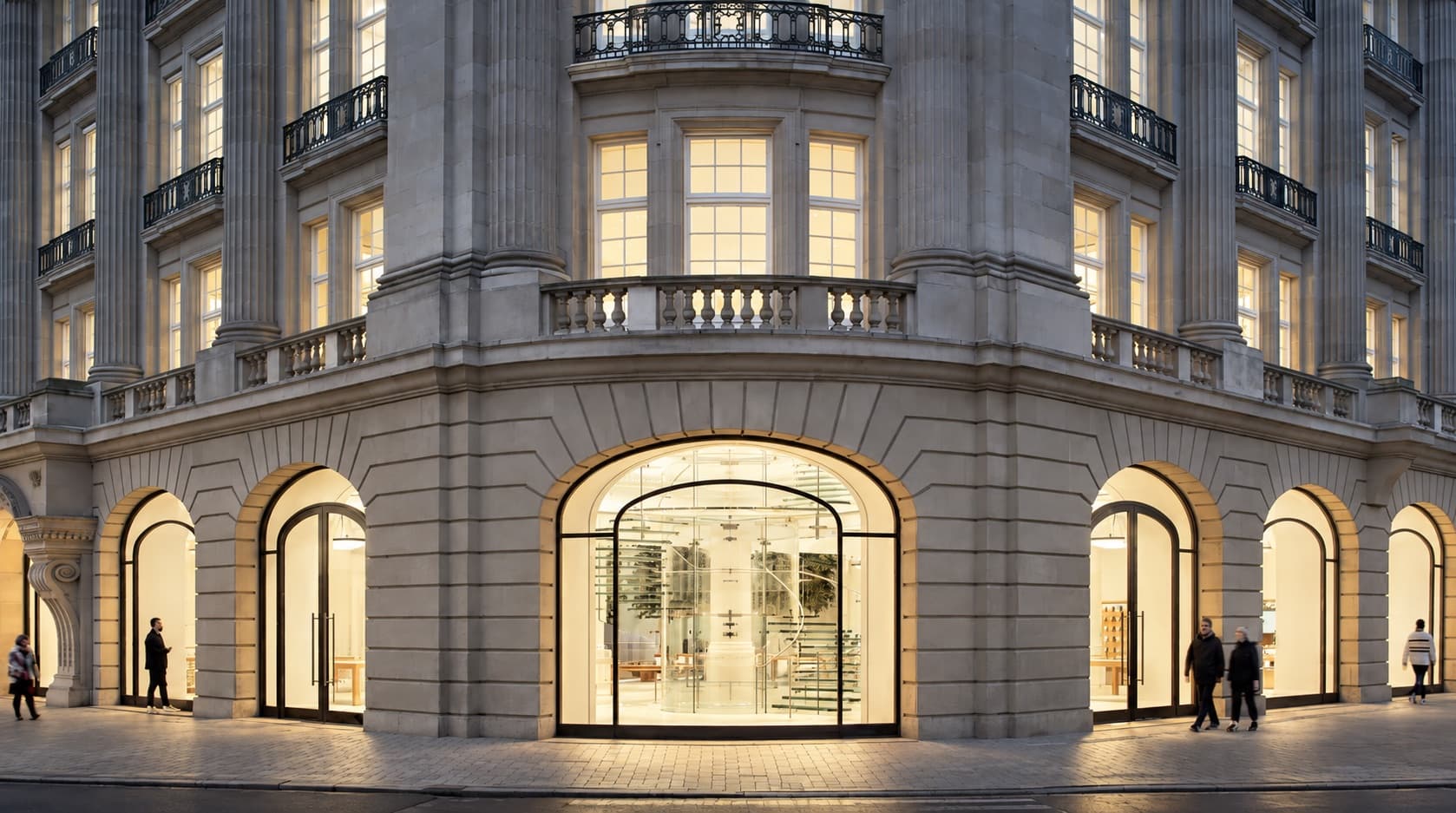 Apple Amsterdam on Leidseplein at dusk, lit arched windows and a glass staircase